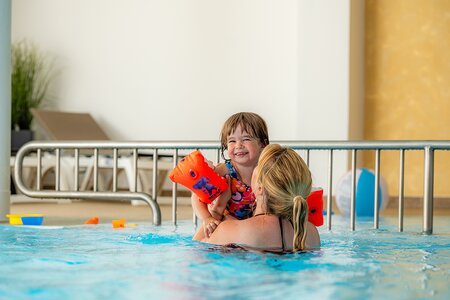 Mädchen am Arm der Mutter im Hallenbad