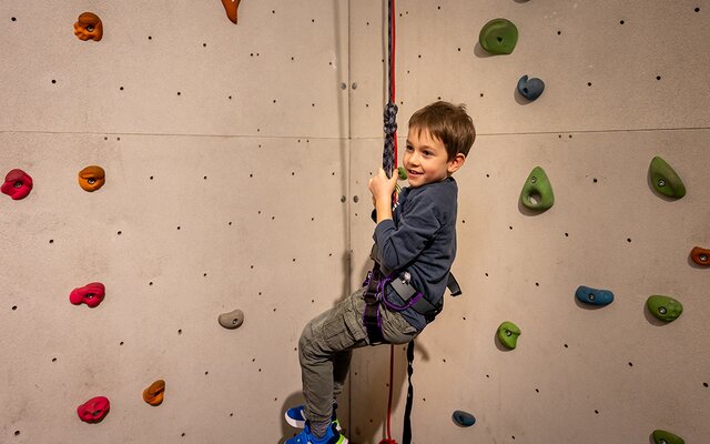 Bub schwingt am Seil in der Kletterwand