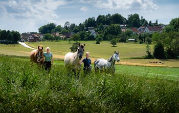 Kind und Frau führen Pferd auf der Wiese