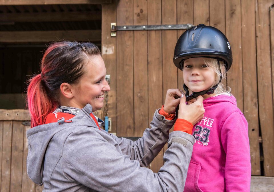 Reitlehrerin setzt Mädchen Helm auf