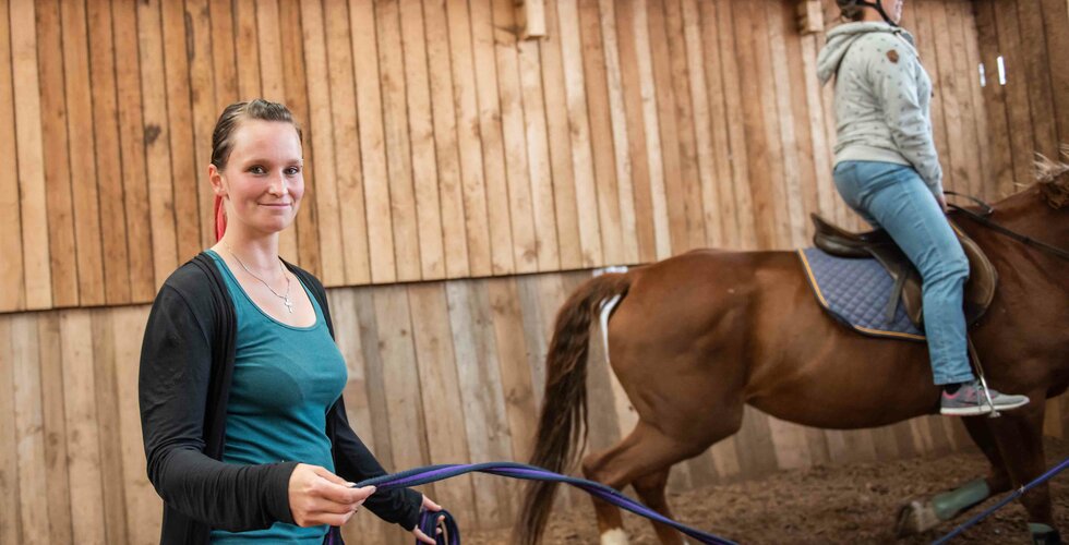 Reitlehrerin führt Pferd in Reithalle